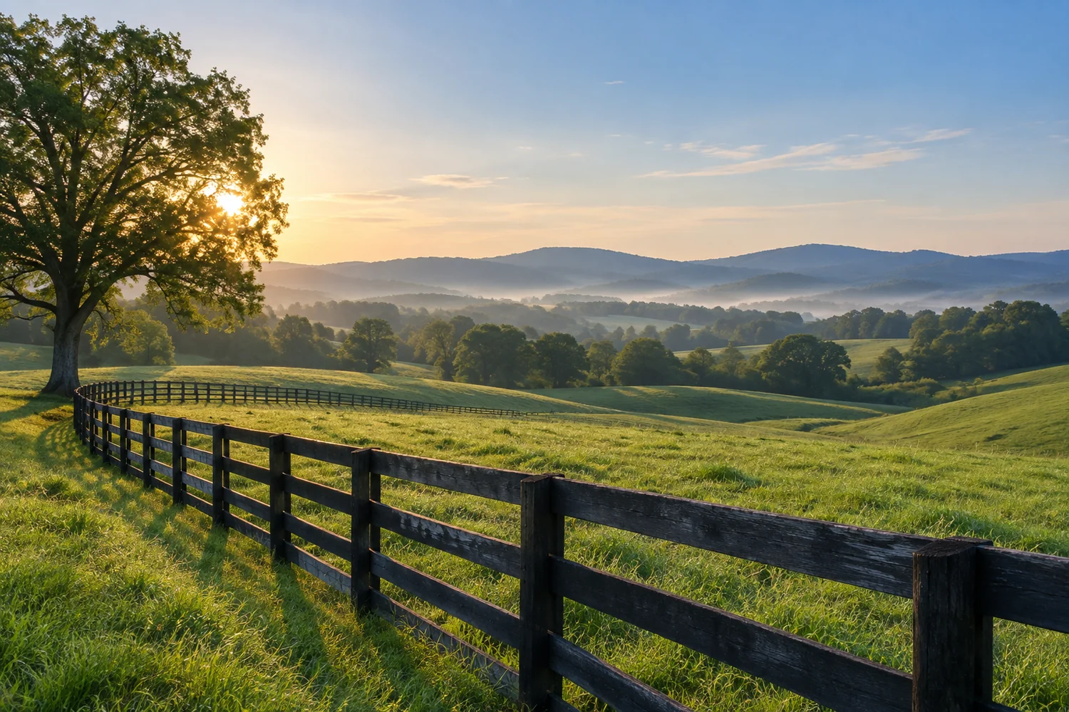 Dark wooden paddock fences lead through rolling green countryside toward hazy blue hills beneath an early-morning sky.
